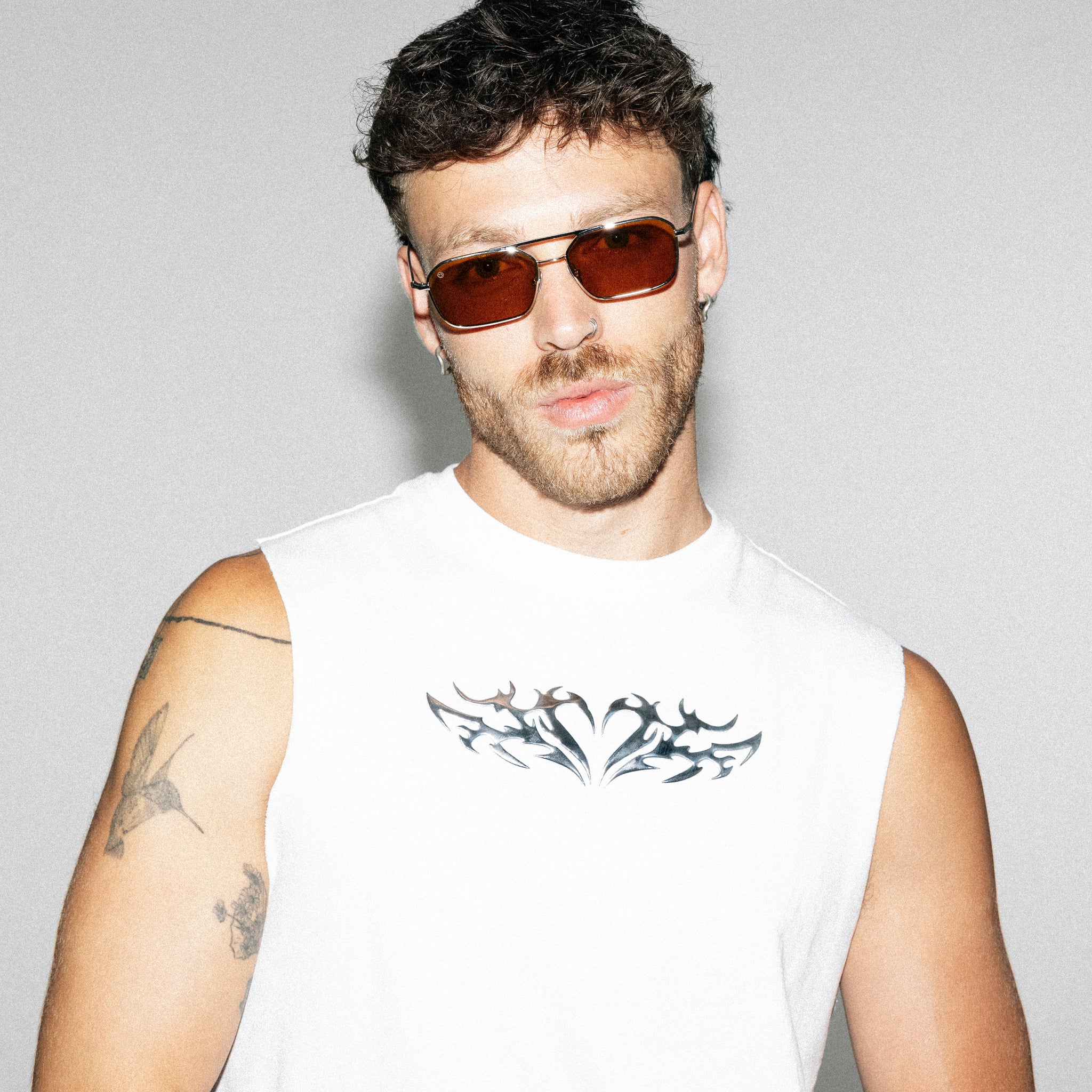 Man wearing sunglasses and a sleeveless white shirt with a black design on a gray background