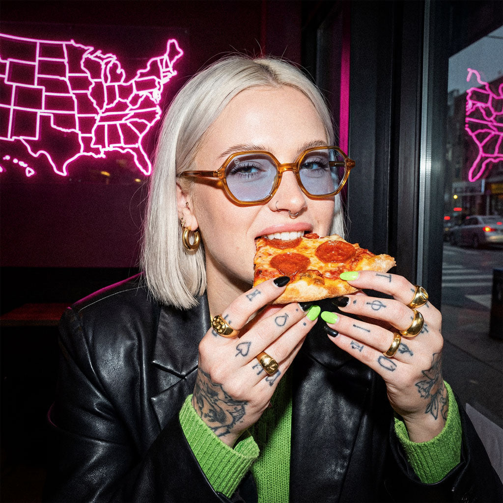 Woman eating pizza in a casual setting with neon signs in the background